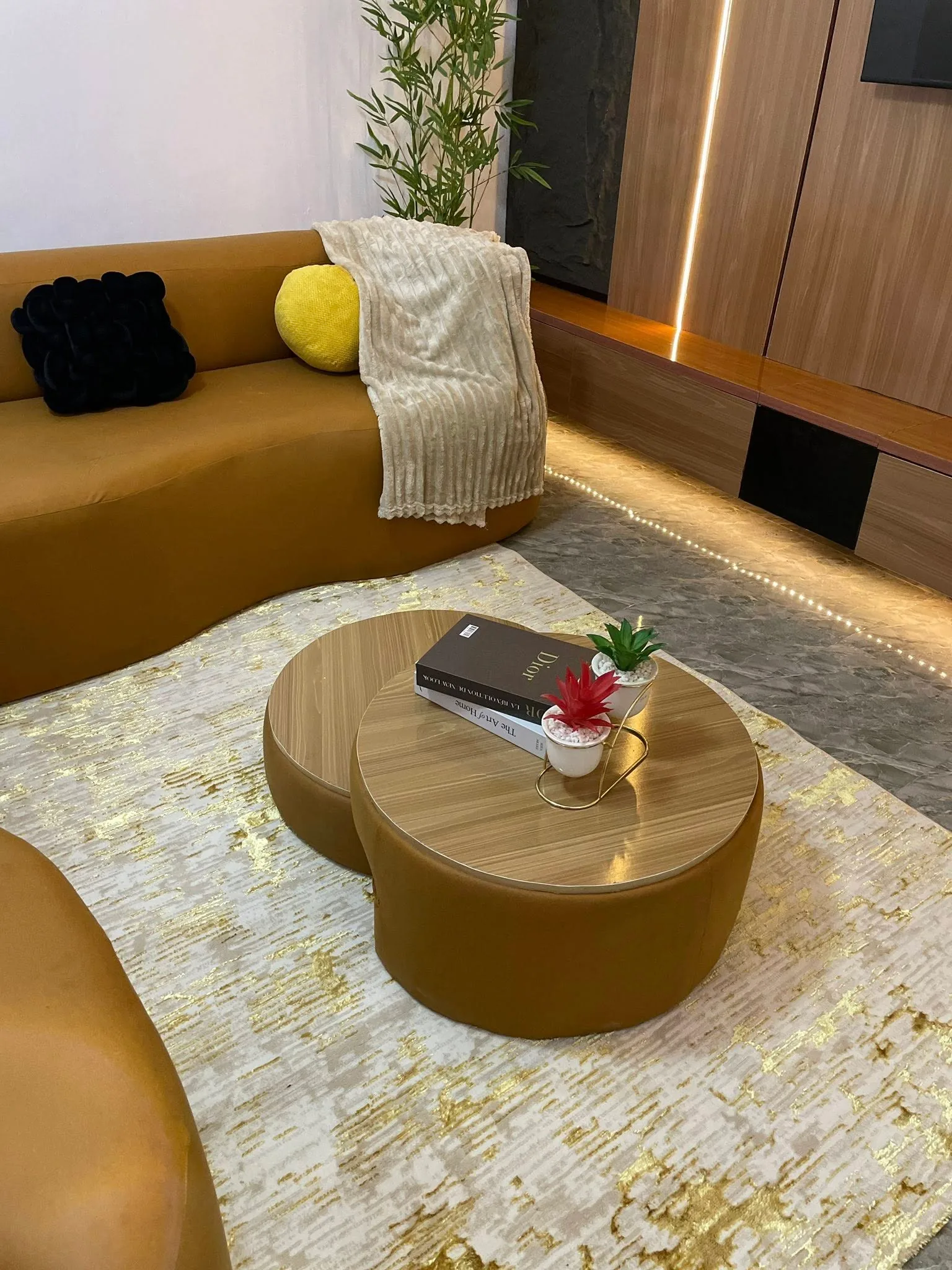 Curved mustard sofa, layered gold-accented rug, and wood nesting tables